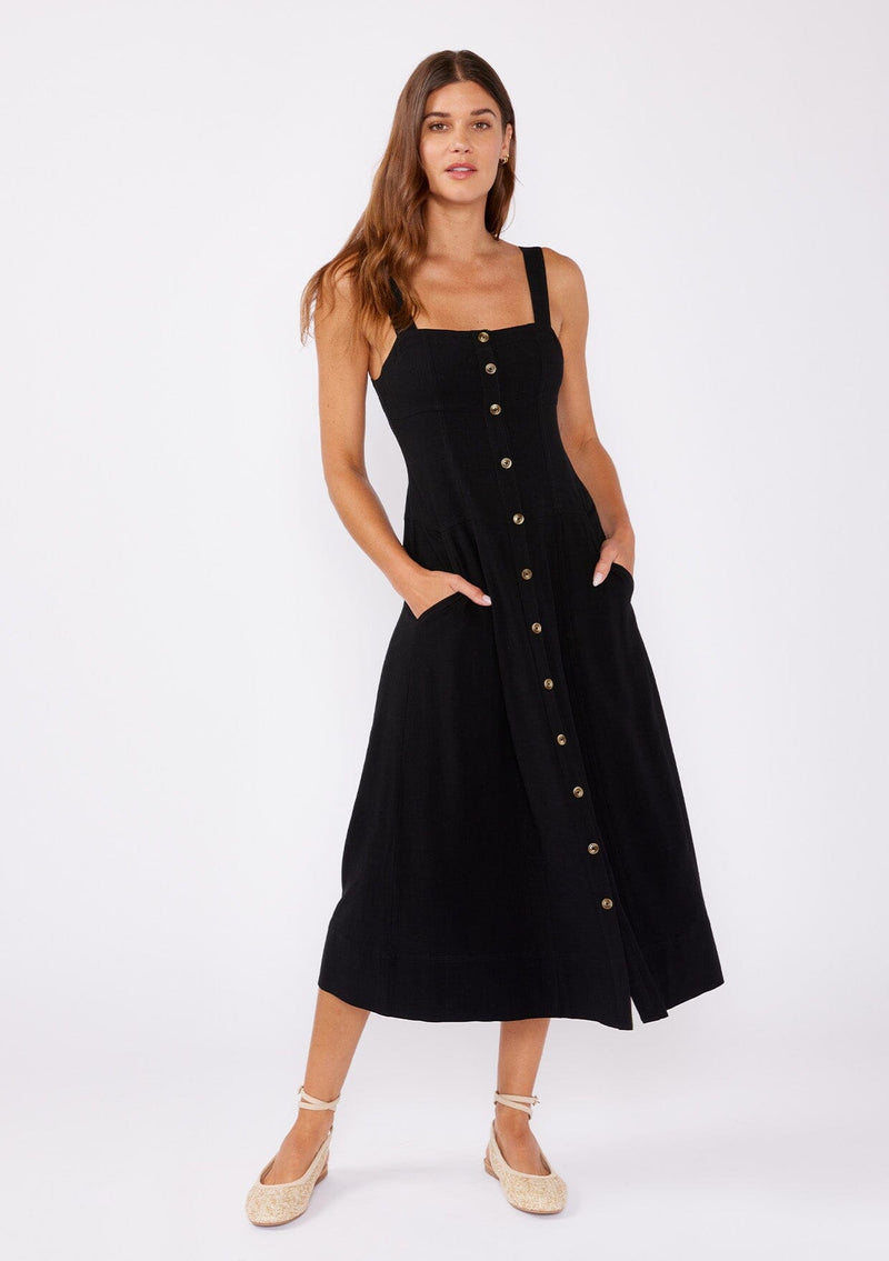 [Color: Black] A brunette model wearing a sleeveless midi dress with a functional  button front and paired with tan ballet flats. A fit and flare dress with a sleeveless design and square neckline. A casual midi dress perfect for daytime activities and running errands. 