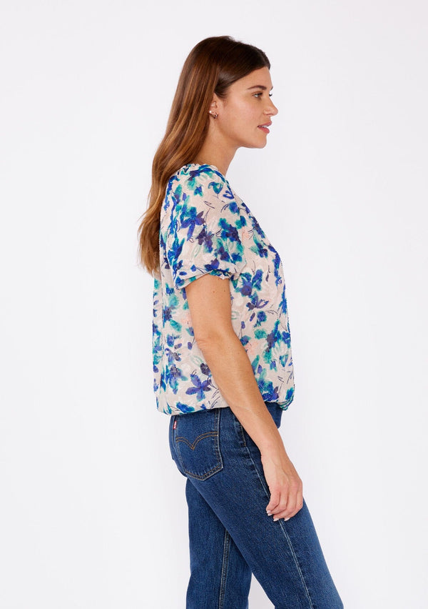 [Color: Natural/Teal] A brunette woman wearing a blue and natural floral chiffon blouse with puff sleeves, decorative button front, and a elastic hem. A summer casual top to wear with denim jeans to dinner or special occasions.