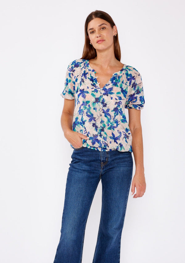 [Color: Natural/Teal] A brunette woman wearing a blue and natural floral chiffon blouse with puff sleeves, decorative button front, and a elastic hem. A summer casual top to wear with denim jeans to dinner or special occasions. 