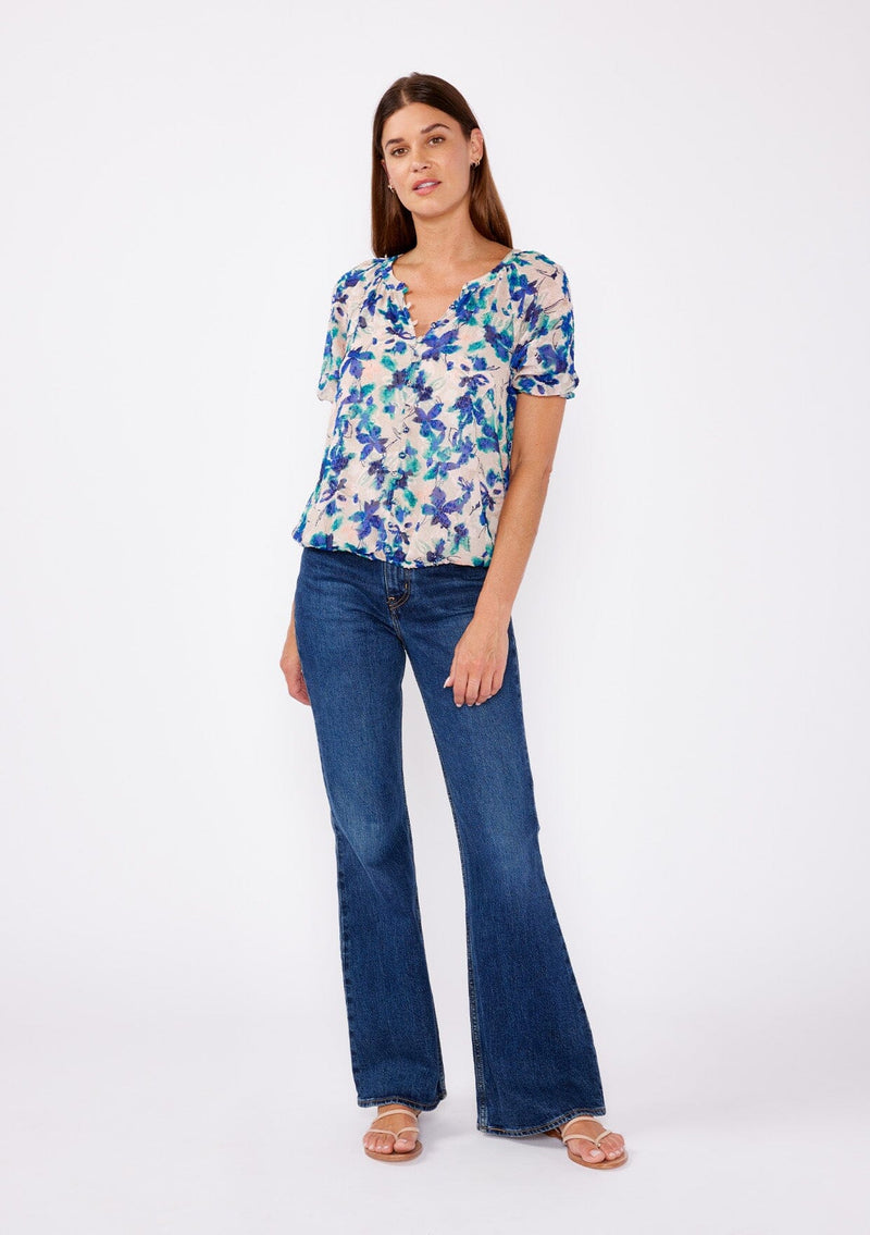 [Color: Natural/Teal] A brunette woman wearing a blue and natural floral chiffon blouse with puff sleeves, decorative button front, and a elastic hem. A summer casual top to wear with denim jeans to dinner or special occasions.