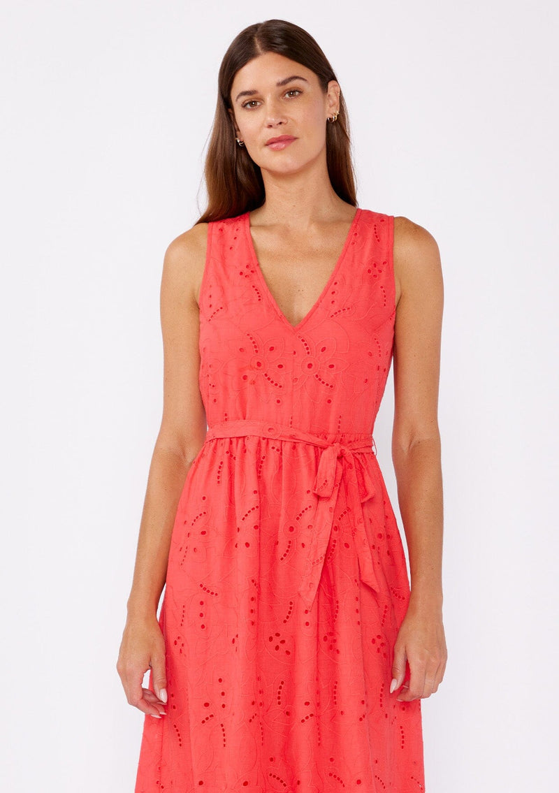 [Color: Coral] A brunette woman wearing a bright coral midi dress with embroidered eyelet details. With a sleeveless design, v neckline, adjustable waist belt, open back with button closure, and a ruffle trimmed hem.