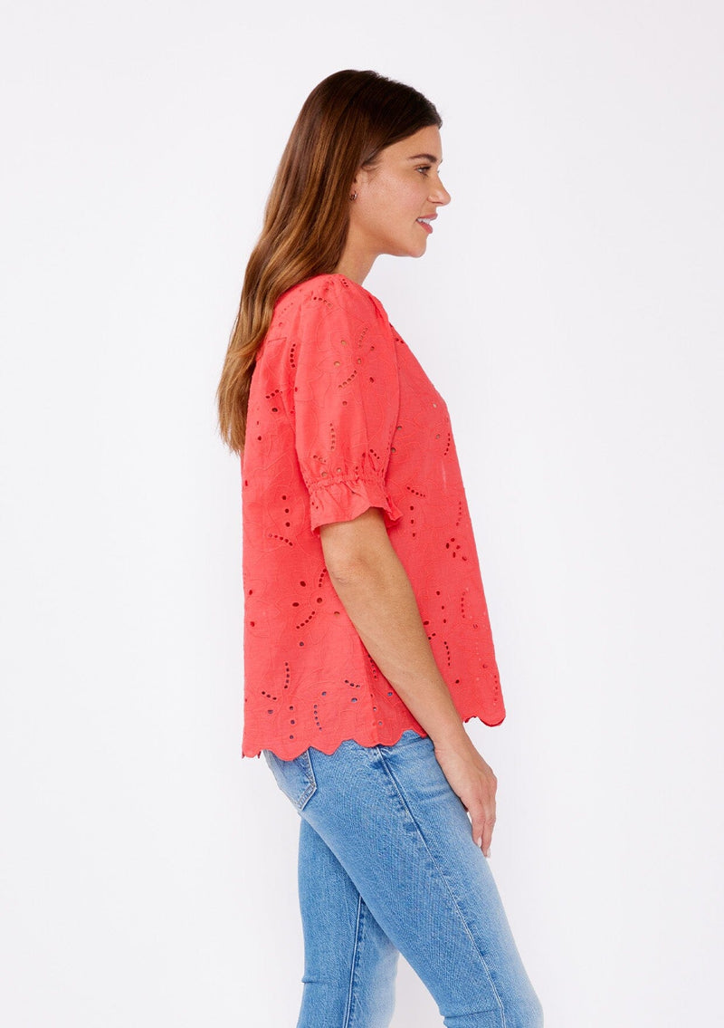 [Color: Coral] A brunette model wearing a coral orange top with a high round neckline, button front, and puff sleeves. Features a ruffled elastic cuff for added flair. A summer top with no lining for a comfortable breezy style for the summer.