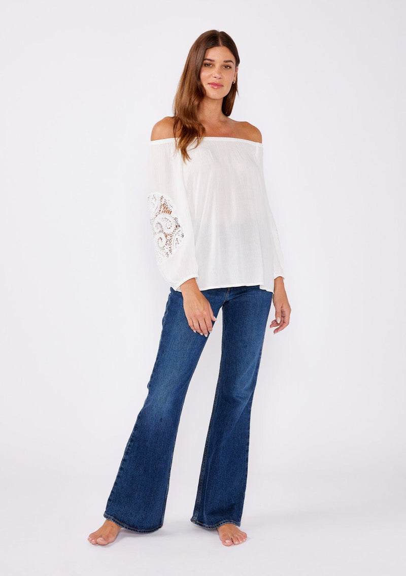 [Color: Off White] A brunette model wearing a casual white blouse with crochet lace detail. A summer top with an elastic neckline for on and off shoulder styling and three quarter length sleeves with elastic cuffs. A relaxed a flowy style perfect for casual outings.