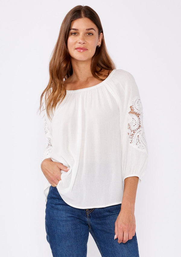 [Color: Off White] A brunette model wearing a casual white blouse with crochet lace detail. A summer top with an elastic neckline for on  and off shoulder styling and three quarter length sleeves with elastic cuffs. A relaxed a flowy style perfect for casual outings. 
