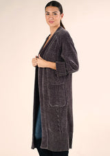 [Color: Charcoal] A side facing image of a brunette model wearing a soft grey chenille knit duster cardigan. With long sleeves, an open front, and side pockets. 