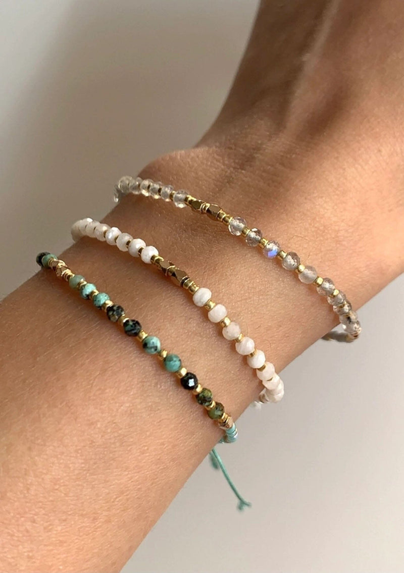 [Color: Labradorite] An adjustable healing bracelet, crafted on a durable nylon cord with gold-plated hardware and clear grey natural gemstones. Designed by Kindred Row.