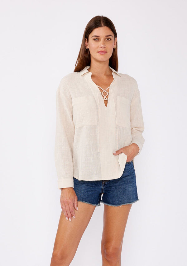[Color: Sand] A relaxed fit blouse crafted from breathable textured cotton fabric. Features a collared neckline, lace up front, and long sleeves with button cuff closures. A daytime casual top for beach outings or running errands. 