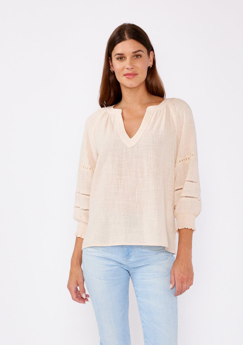 [Color: Natural] A brunette model wearing a textured cotton blouse for summer. Features a split v neckline, three quarter length sleeve, smocked cuff, and delicate lace trim inserts. A breathable and stylish cotton blouse for any occasion. 