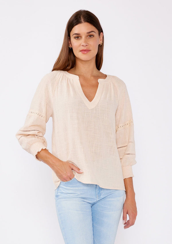[Color: Natural] A brunette model wearing a textured cotton blouse for summer. Features a split v neckline, three quarter length sleeve, smocked cuff, and delicate lace trim inserts. A breathable and stylish cotton blouse for any occasion. 