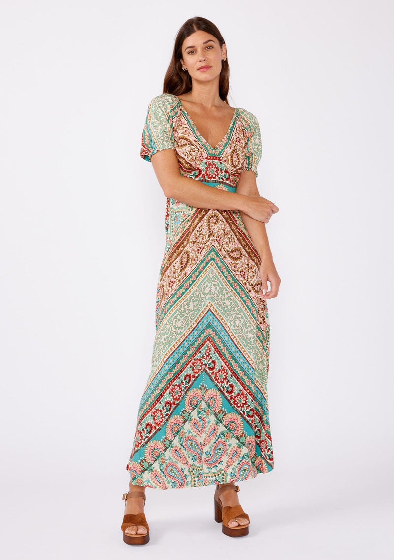 [Color: Jade/Natural] An image of a brunette model wearing a multi print bohemian maxi dress with brown heels for the fall season. A teal and green flowy dress with a v neckline, puff sleeves, and smocked back. A popular maxi dress for easy transition from summer to fall. 