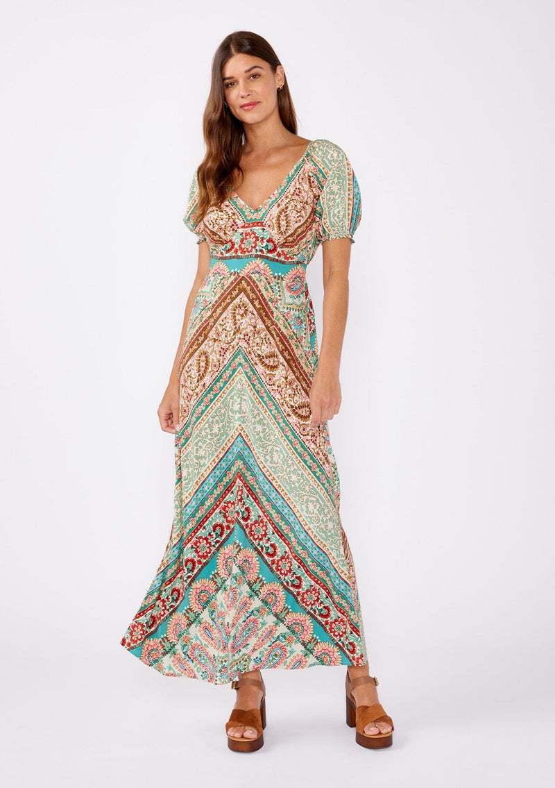 [Color: Jade/Natural] An image of a brunette model wearing a multi print bohemian maxi dress with brown heels for the fall season. A teal and green flowy dress with a v neckline, puff sleeves, and smocked back. A popular maxi dress for easy transition from summer to fall. 