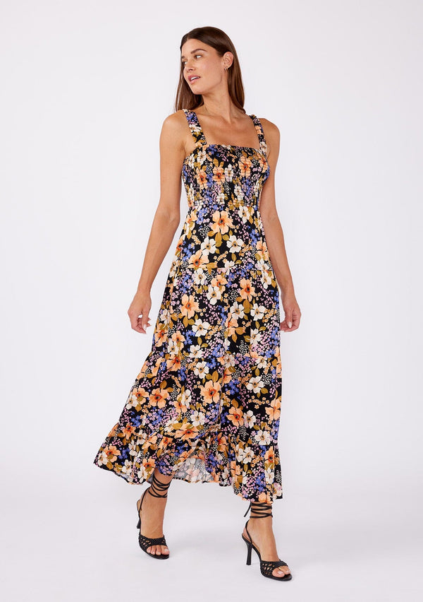 [Color: Black/Dusty Coral] A brunette woman wearing an all over purple and black floral print dress with black heels. A stunning tiered maxi with elastic straps, square neckline,  and a smocked bust. A perfect day to  night dress for many occasions. 