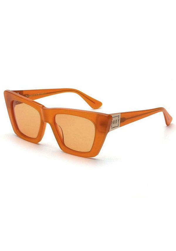 [Color: Apricot] A pair of oversized clear orange plant-based acetate frames with amber lenses, from INDY. 