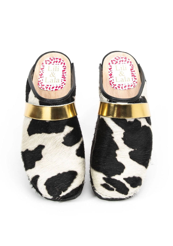 [Color: Cowhide/Gold] A black and white cowhide classic clog with gold strap and a rubber sole. Handmade in Sweden.