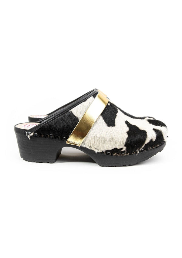 [Color: Cowhide/Gold] A black and white cowhide classic clog with gold strap and a rubber sole. Handmade in Sweden.