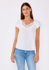 [Color: Chalk] Crafted in a soft white hue, this top features flattering cap sleeves and a delicate lace-trimmed V-neckline, adding a touch of feminine charm. The lightweight fabric drapes beautifully, offering a relaxed yet polished look that's ideal for any occasion. Pair it with your favorite denim for a casual day out or dress it up with a skirt for a chic evening ensemble. Embrace timeless style with this versatile and sophisticated piece.