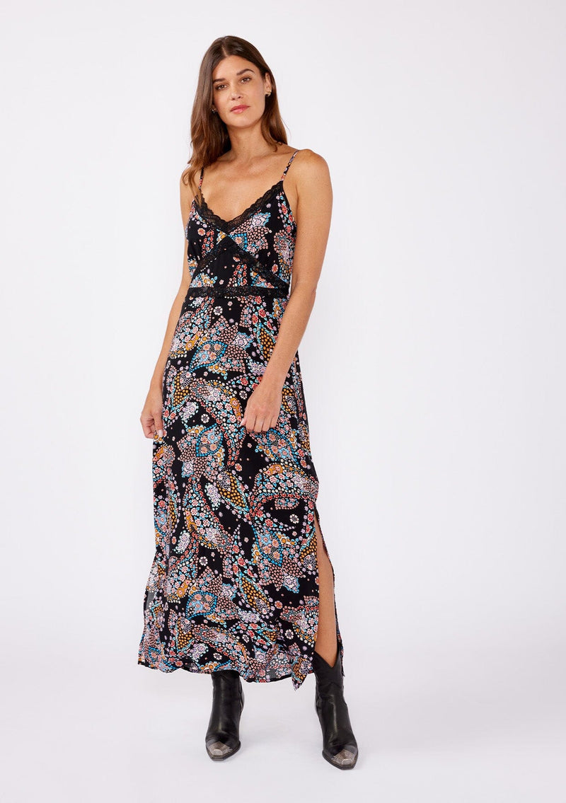 [Color: Black/Light Blue] A brunette model wearing a multi color floral print maxi dress with a flirty lace trim. An edgy bohemian maxi dress with a flattering v neckline, adjustable spaghetti straps, smocked back, and side slits. A sleeveless dress perfectly paired with boots or flats for the summer to fall season.