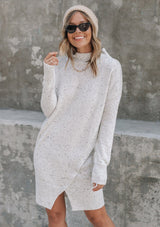 [Color: Silver] A woman standing outside wearing a mélange knit sweater dress. Featuring a mock neckline, long sleeves with contrast ribbed details, and an asymmetric front slit detail.