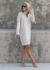 [Color: Silver] A woman standing outside wearing a mélange knit sweater dress. Featuring a mock neckline, long sleeves with contrast ribbed details, and an asymmetric front slit detail.