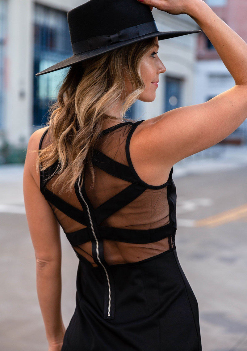 [Color: Black] A model wearing a black bodycon mini dress with sheer yoke detail and exposed back zip detail. 