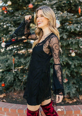 [Color: Black] A woman wearing a black mini dress with long lace bell sleeves and a scoop neckline. 