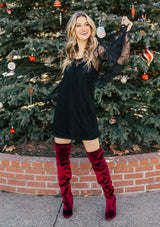 [Color: Black] A woman wearing a black mini dress with long lace bell sleeves and a scoop neckline. 