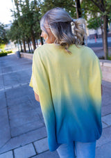 [Color: Lemon] A blond woman wearing an ombre tie dye sweater top. Features a scooped neckline, breezy side vents and front pockets. 