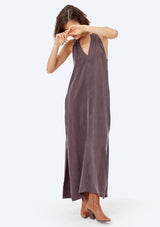 [Color: Charcoal] A brunette model wearing a cupro maxi dress with a split v-neckline, side pockets, and side slits. 