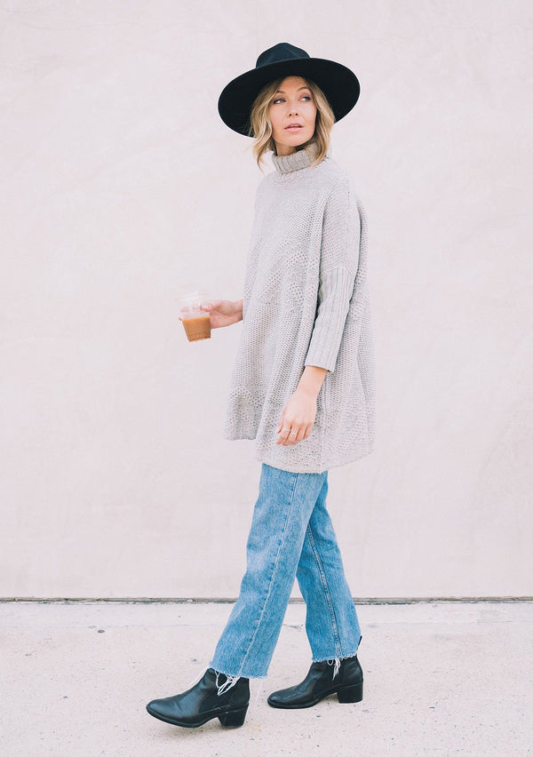 [Color: Heather Grey] A woman wearing a cable knit pullover. Featuring contrast ribbed sleeves and turtleneck, a relaxed, oversize fit and tunic style length, and flattering three quarter length dolman sleeves.