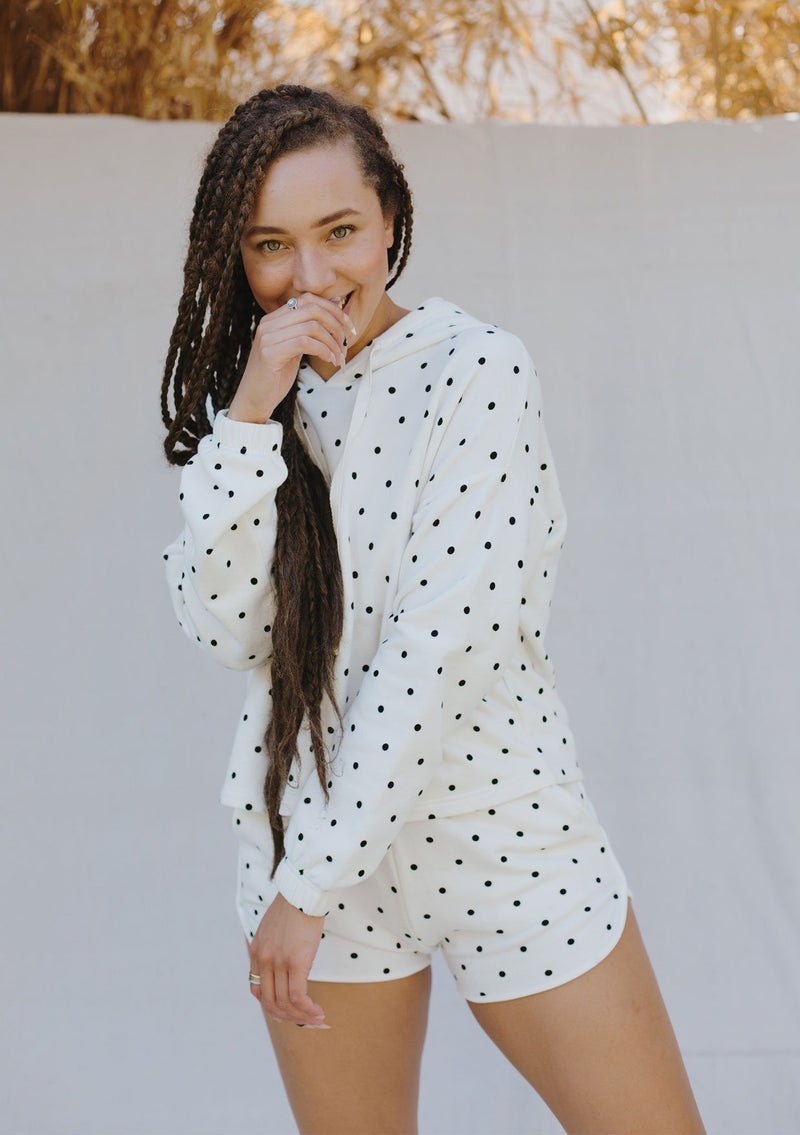 [Color: Ivory/Black] A woman standing outside wearing a cropped polka dot pullover hoodie. Featuring long sleeves with elastic cuffs and a drawstring hoodie. 