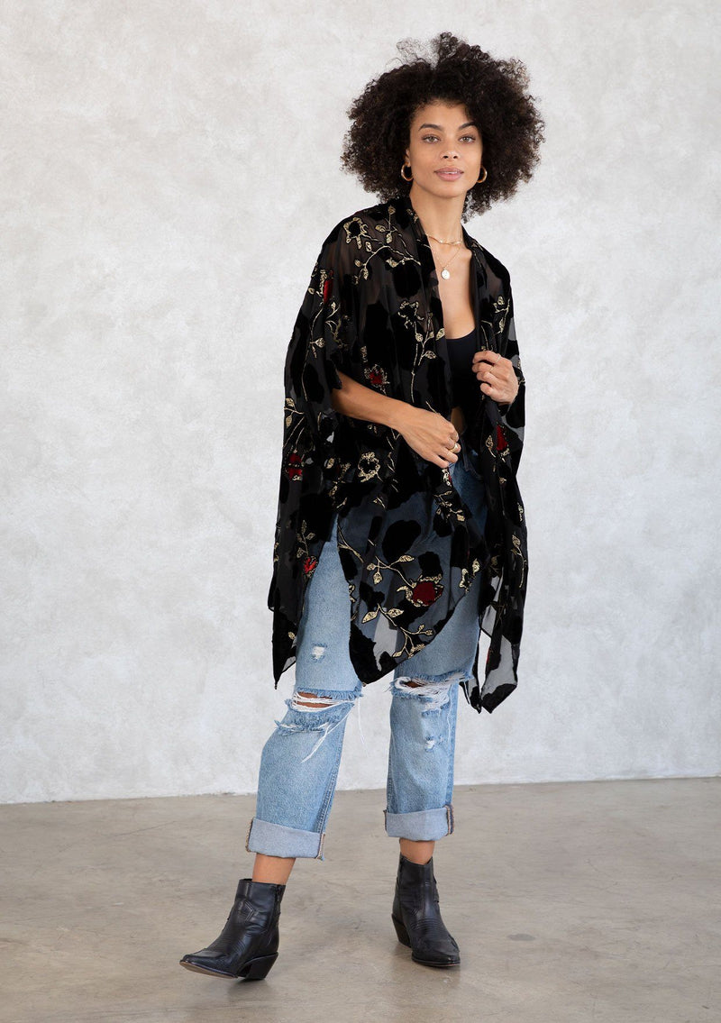 [Color: RedFloral/Black] A model wearing a holiday ready bohemian velvet kimono in black and red floral. With gold thread design, an open front, and half length sleeves. 