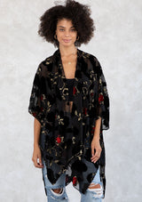 [Color: RedFloral/Black] A model wearing a holiday ready bohemian velvet kimono in black and red floral. With gold thread design, an open front, and half length sleeves. 