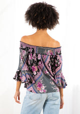 [Color: Black/Orchid] A model wearing a floral patchwork blouse. With three quarter length sleeves and a flounced cuff, a billowy relaxed fit, and a smocked elastic off shoulder detail. 