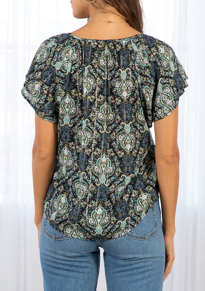 [Color: Black/Teal] A model wearing a black and teal paisley print bohemian top with gold lurex thread detail. Featuring a double flutter short sleeve, a self covered button front, and a split neckline with tassel ties. 