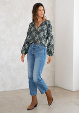 [Color: Black/Teal] A model wearing a black and teal paisley print peasant blouse with gold lurex thread details. With long voluminous sleeves, a self covered button front, and a button loop trimmed v neckline. 