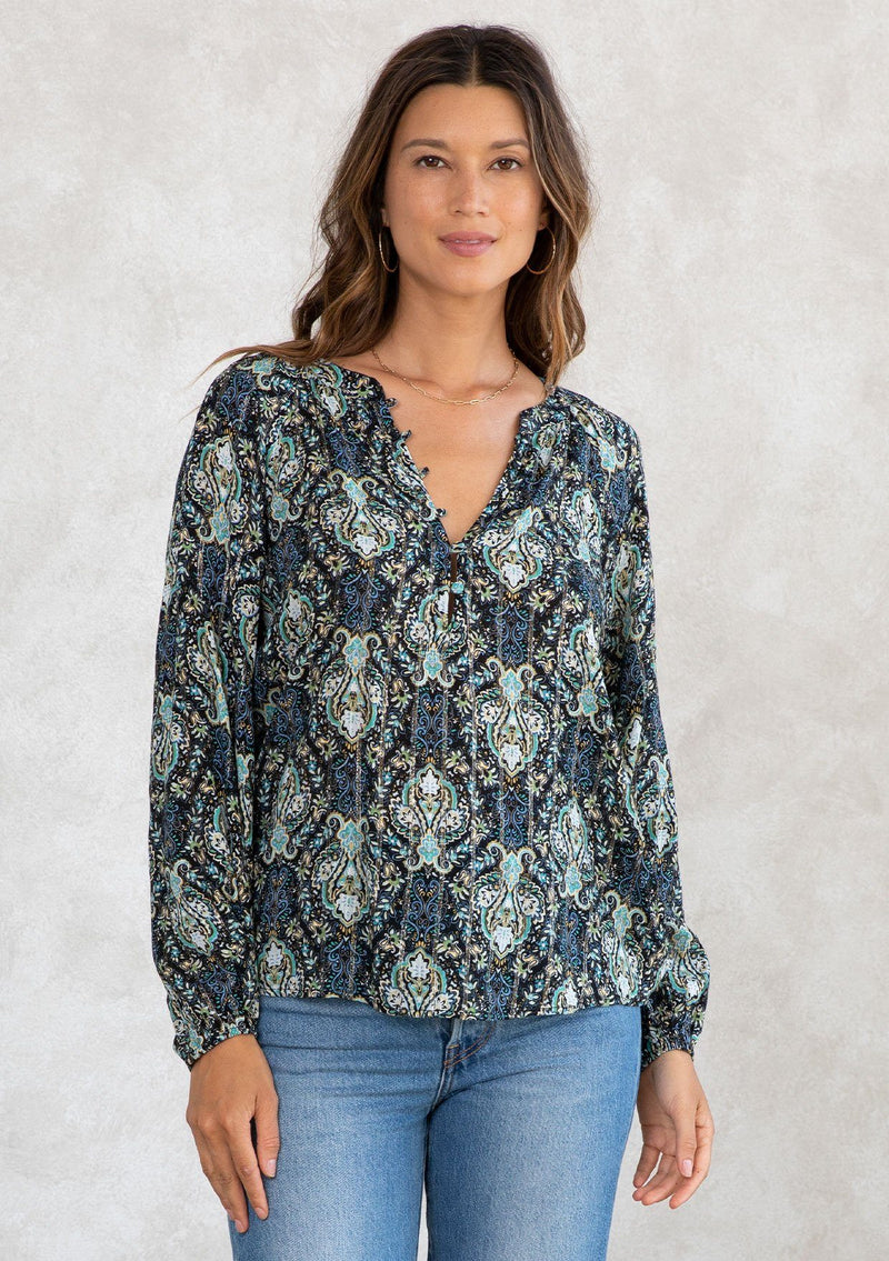 [Color: Black/Teal] A model wearing a black and teal paisley print peasant blouse with gold lurex thread details. With long voluminous sleeves, a self covered button front, and a button loop trimmed v neckline. 