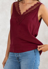 [Color: Merlot] A model wearing a merlot red camisole tank top. With a lace trim v neckline in front and back and a relaxed fit. 