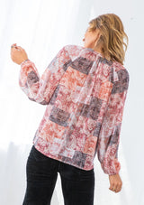 [Color: Natural/Rose] A model wearing a peasant blouse in a red paisley patchwork print. With a loop button front, long voluminous sleeves, elastic wrist cuffs, and a banded collar. 