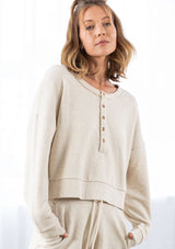 [Color: Seashell] A model wearing a cropped beige pullover sweatshirt with a buttoned front detail. With long raglan sleeves and a round neckline with raw unfinished hem.