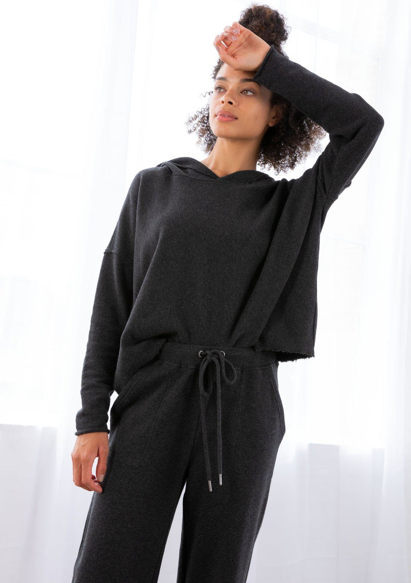 [Color: Black] A model wearing a black cropped hoodie. With a raw edge hemline and a long sleeve with dropped shoulder.