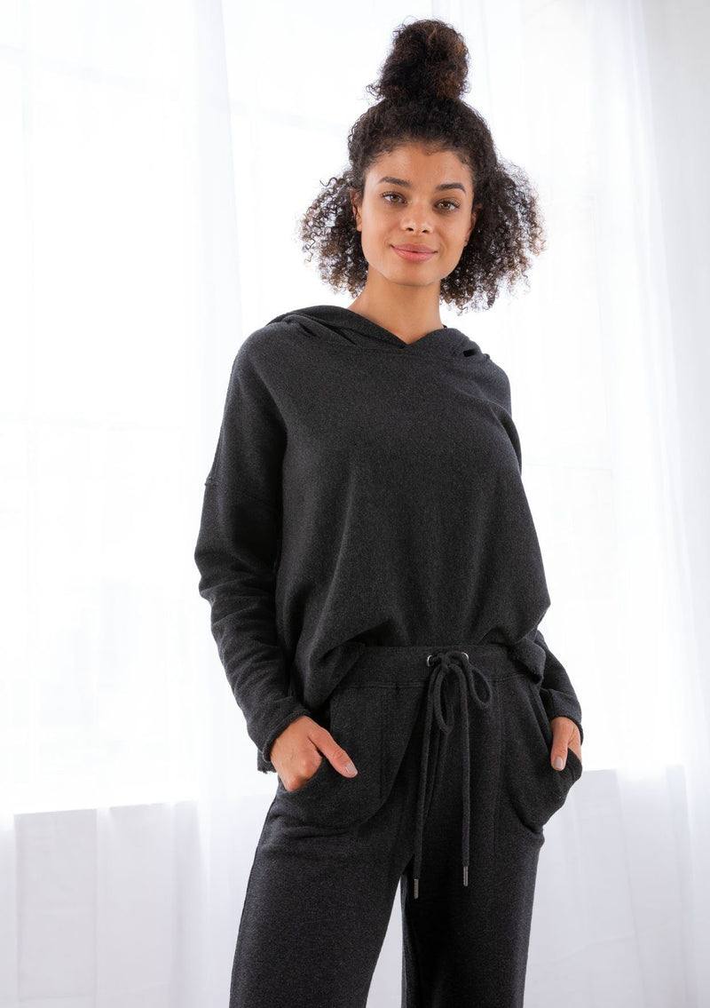 [Color: Black] A model wearing a black cropped hoodie. With a raw edge hemline and a long sleeve with dropped shoulder.