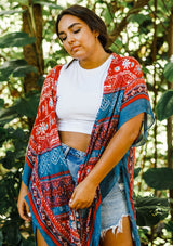 [Color: Blue/Brick] A model wearing a red and blue bohemian mid length kimono. Featuring half length kimono sleeves, side slits, an open front, and a multi colored pattern throughout.