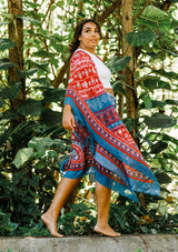 [Color: Blue/Brick] A model wearing a red and blue bohemian mid length kimono. Featuring half length kimono sleeves, side slits, an open front, and a multi colored pattern throughout.