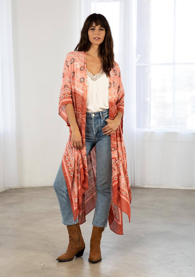 [Color: Brick/Coral] A model wearing a red and coral bohemian mid length kimono. Featuring half length kimono sleeves, side slits, an open front, and a multi colored pattern throughout.