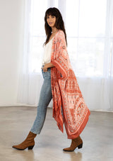 [Color: Brick/Coral] A model wearing a red and coral bohemian mid length kimono. Featuring half length kimono sleeves, side slits, an open front, and a multi colored pattern throughout.