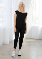 [Color: Black] A model wearing a classic black athleisure tank top. With a boat neckline, a gathered detail along the left shoulder, and a boxy fit.