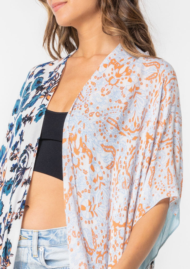 [Color: Lt Blue/Sand] A model wearing a stunning mid length kimono in a light blue mixed floral print. Featuring half length kimono sleeves, side slits, and an open front.