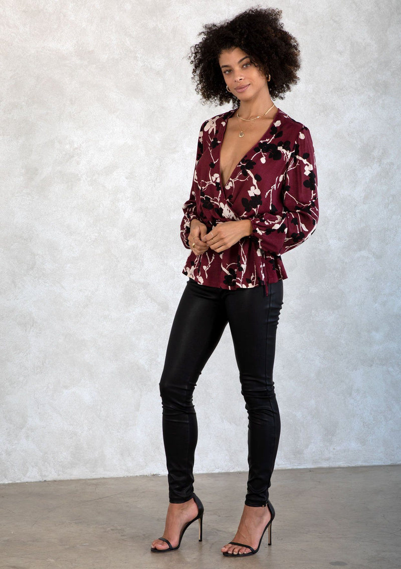 [Color: Merlot/Ivory] A model wearing a dark red and ivory floral print blouse. With a mini pom trimmed surplice neckline, voluminous long sleeves, an adjustable drawstring waist with side ties, and a peplum waist. 