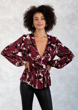 [Color: Merlot/Ivory] A model wearing a dark red and ivory floral print blouse. With a mini pom trimmed surplice neckline, voluminous long sleeves, an adjustable drawstring waist with side ties, and a peplum waist. 