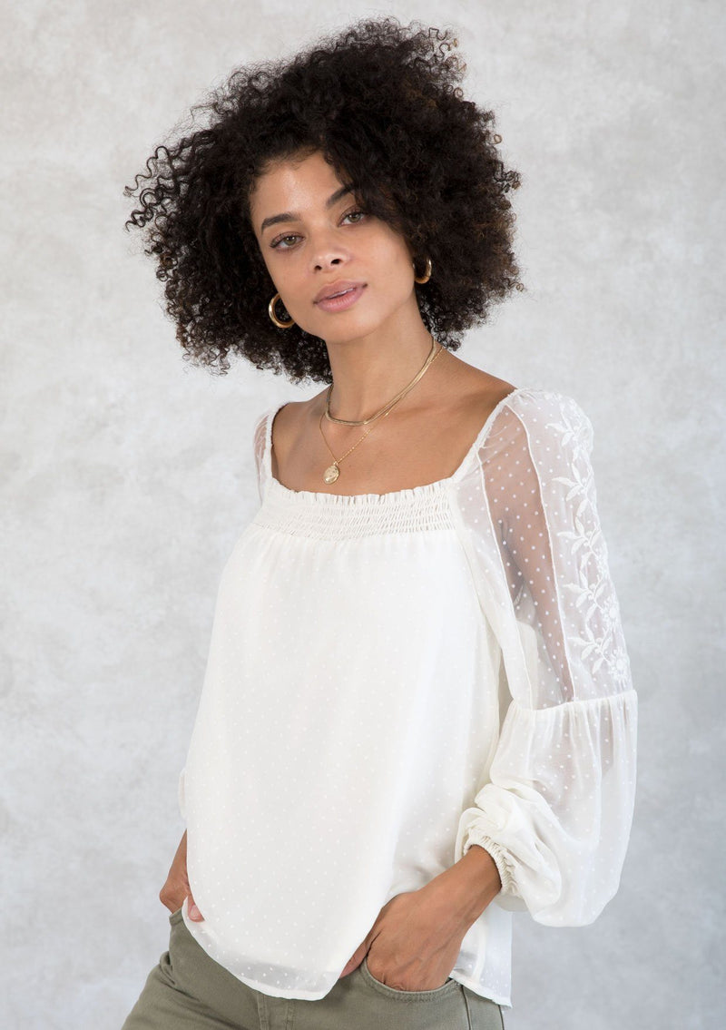 [Color: Ivory] A model wearing a romantic square neck blouse in an ivory dot chiffon. With a long voluminous lantern sleeve with embroidered dot mesh detail and a billowy relaxed fit. 